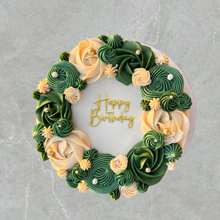 Ein Geburtstagskuchen mit grünen und gelben Zuckergussblumen und Blättern, mit 'Happy Birthday' in Gold geschrieben.