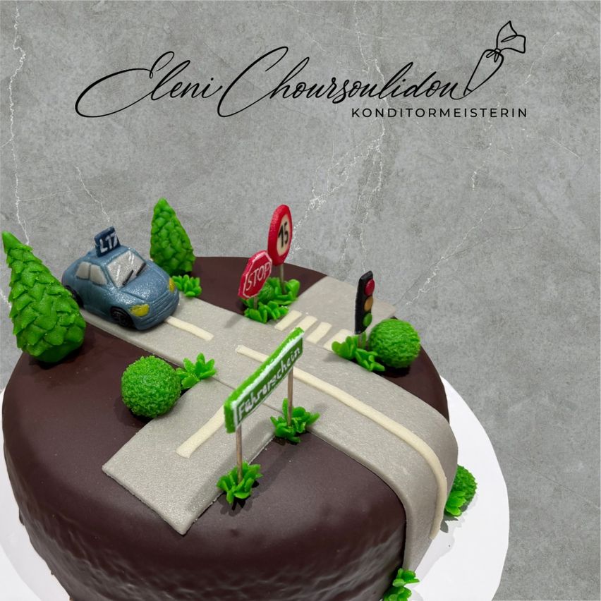 Ein Schokoladenkuchen, der wie eine Straße mit einem Auto und Stoppschildern aussieht. Der Kuchen hat Bäume und Büsche um die Straße herum. Er steht auf einem weißen Teller.