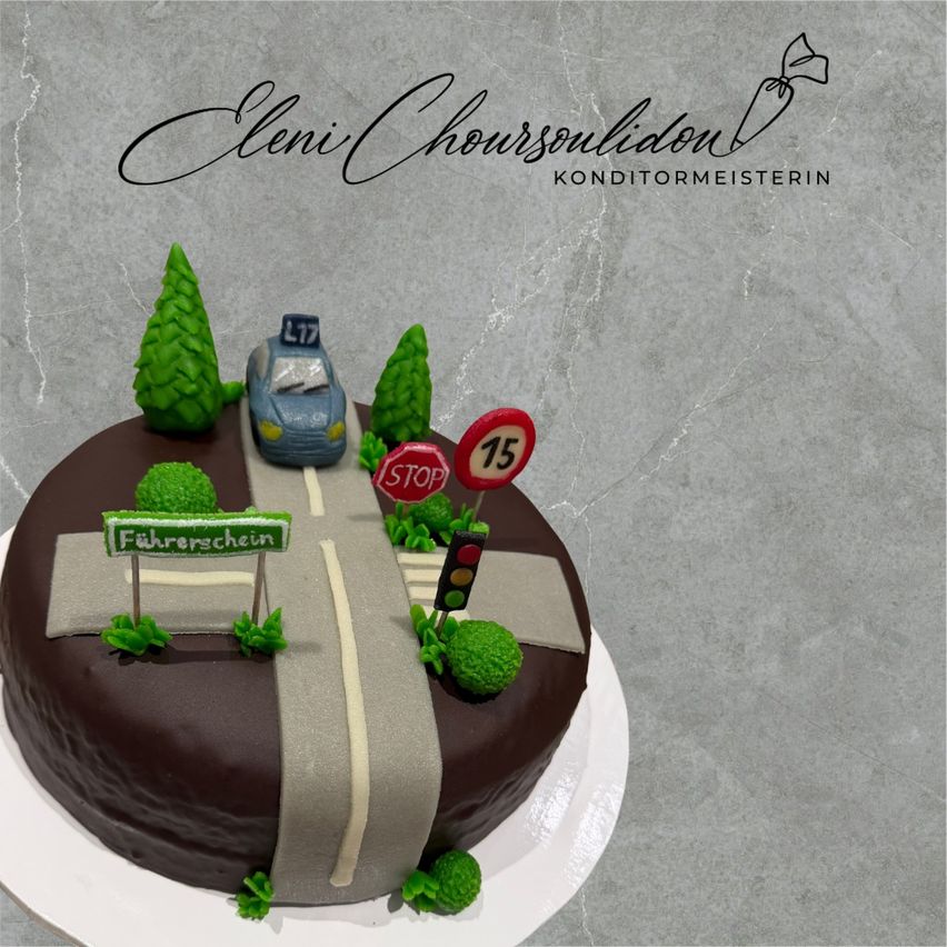 Ein Schokoladenkuchen in Form einer Straße mit einem Auto und einem Stoppschild. Er ist mit Bäumen und einer Ampel dekoriert. Der Kuchen hat ein Schild mit der Aufschrift 'Fahrerschein'.