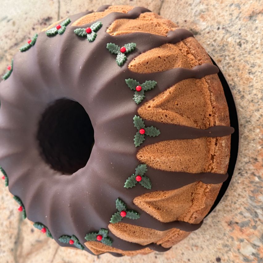 Ein mit Schokolade überzogener Bundtkuchen mit roten Beeren und grünen Blättern darauf steht auf einer Marmoroberfläche.