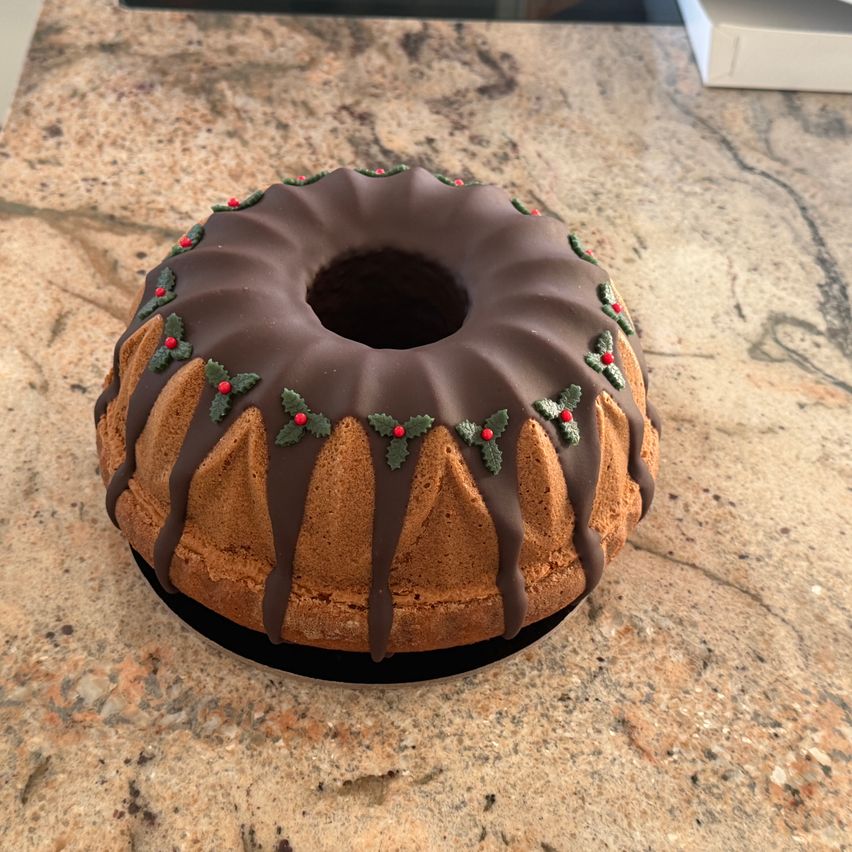Ein mit Schokolade überzogener Bundkuchen mit einem Loch in der Mitte, dekoriert mit Schokoladensauce und grünen Blättern. Er steht auf einer Marmorarbeitsplatte.