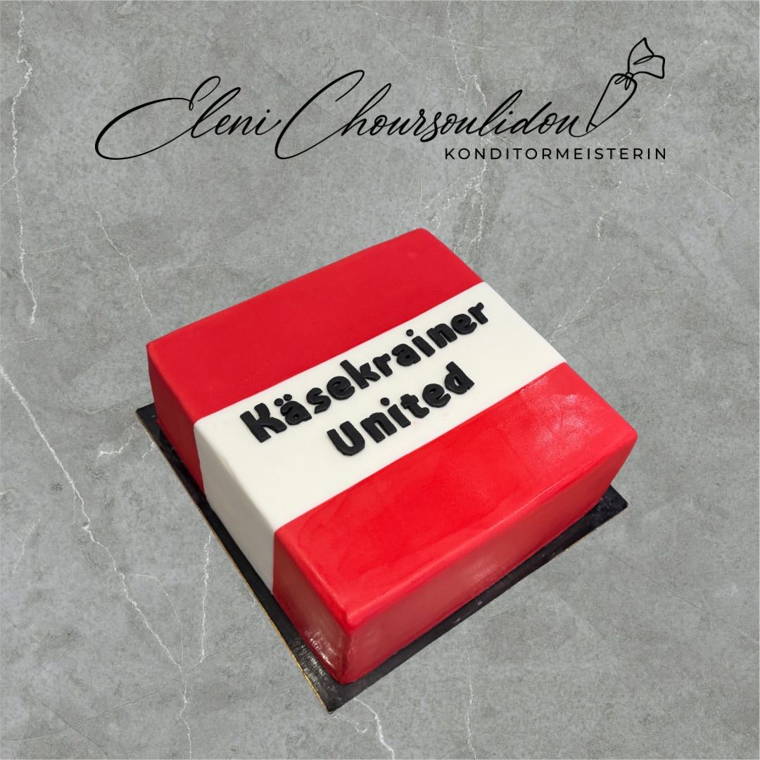Ein rot-weißer Kuchen mit der Aufschrift 'Kaiserkrainer United' steht auf einer Marmoroberfläche. Der Kuchen hat ein Band darum geschlungen.
