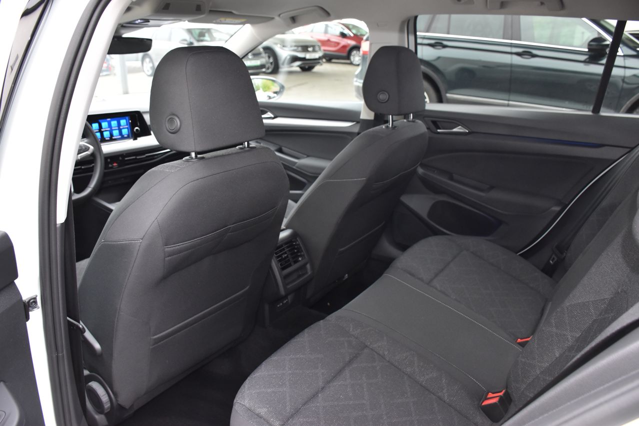 Der Innenraum eines Autos mit zwei grauen Sitzen und einem digitalen Armaturenbrett-Display. Andere Autos sind durch die Fenster sichtbar.