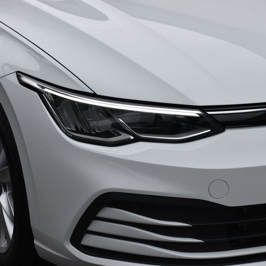 Nahaufnahme der vorderen Stoßstange eines weißen Autos mit LED-Scheinwerfern, schwarzer Kühlergrill und schlankem Design.