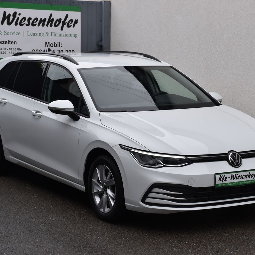 Ein weißer Volkswagen-Fahrzeug ist vor einem Gebäude mit einem Schild, das Wiesenhofer und Dienstleistungen anzeigt, geparkt.