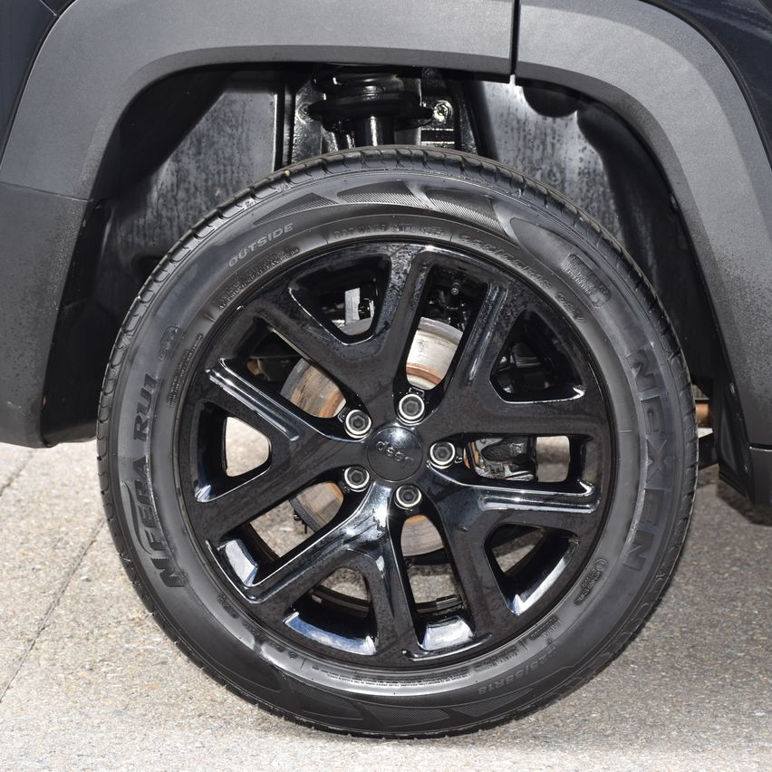 Nahaufnahme eines schwarzen SUV-Rades mit einem glänzenden schwarzen Alufelgen und einem schwarzen Reifen. Das Rad hat eine silberne Radkappe und der Kotflügel des Autos ist im Hintergrund sichtbar.