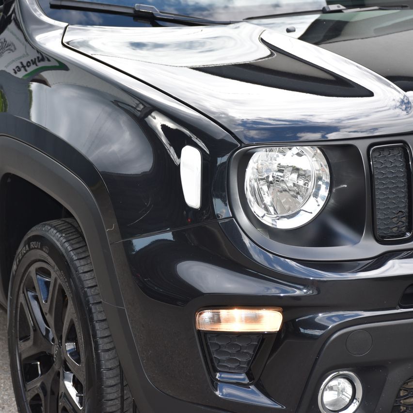 Nahaufnahme eines schwarzen Jeep Renegade mit poliertem Frontstoßfänger, Scheinwerfern und Kühlergrill. Der Reifen und Felge sind ebenfalls sichtbar.