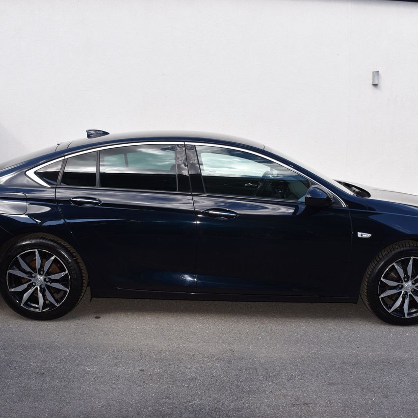 Ein dunkelblauer Sedan mit Leichtmetallrädern steht vor einer weißen Wand.