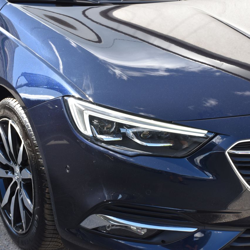 Eine Nahaufnahme der Vorderseite eines blauen Autos zeigt schlanke Scheinwerfer, eine glänzende Motorhaube und ein poliertes Leichtmetallrad. Das aerodynamische Design und die moderne Ästhetik des Autos werden hervorgehoben.
