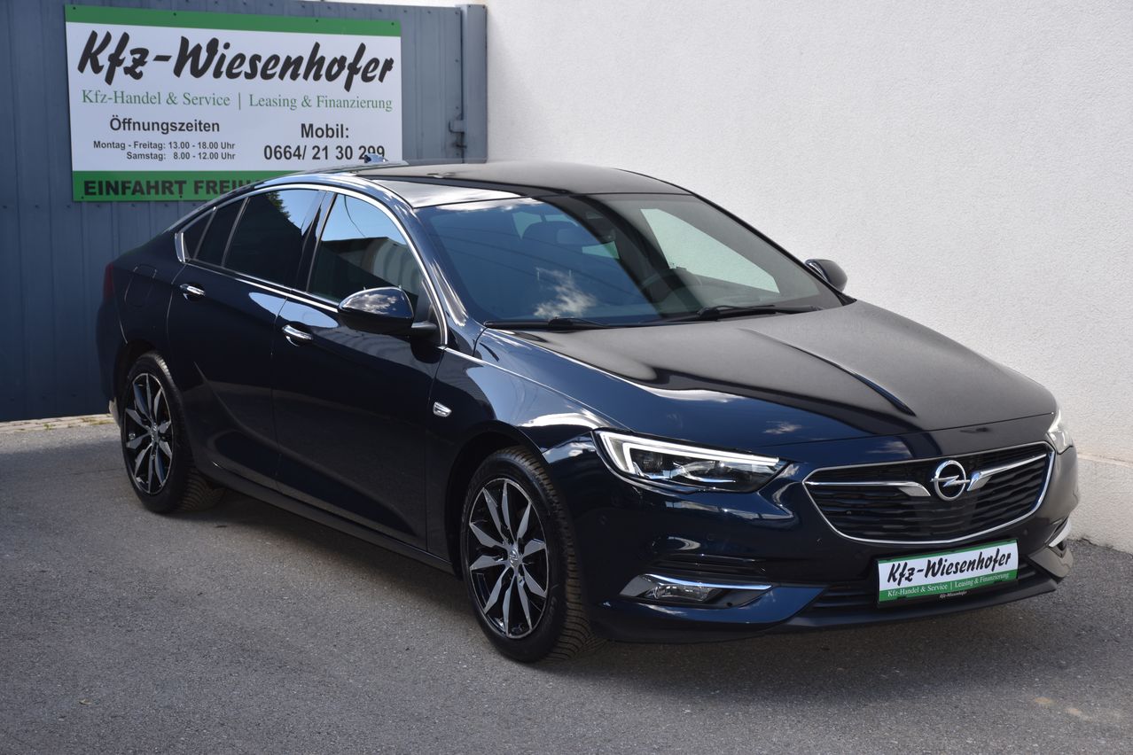 Ein dunkelblauer Opel Astra ist vor einem Gebäude mit einem grünen Schild, auf dem Wiesenhofer steht, geparkt. Das Auto hat ein Nummernschild mit der Aufschrift KFz-W.