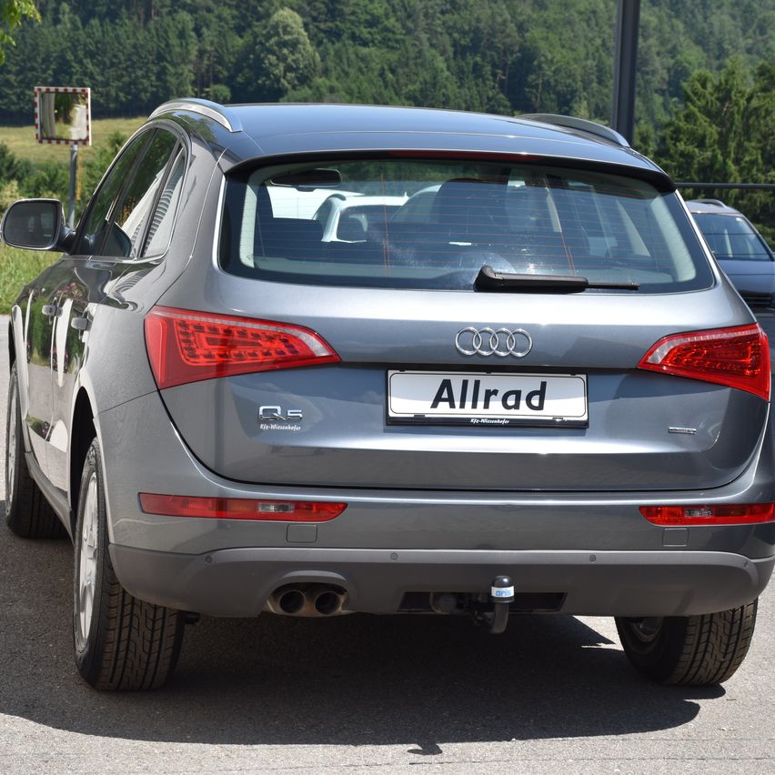 Die Heckseite eines silbernen Audi Q5 SUV ist auf einem Parkplatz abgestellt. Das Kennzeichen lautet 'Allrad'.