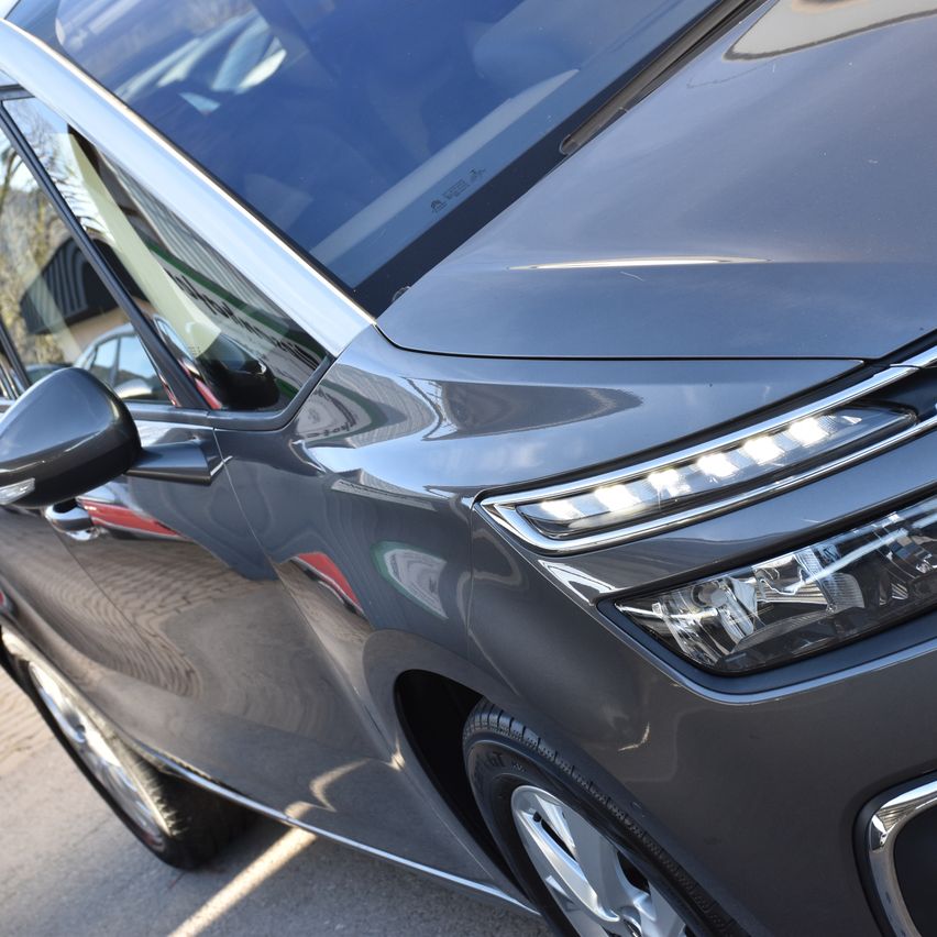 Eine Nahaufnahme der dunklen grauen Vorderseite eines Autos mit schlanken Scheinwerfern und einer polierten Oberfläche an einem sonnigen Tag.