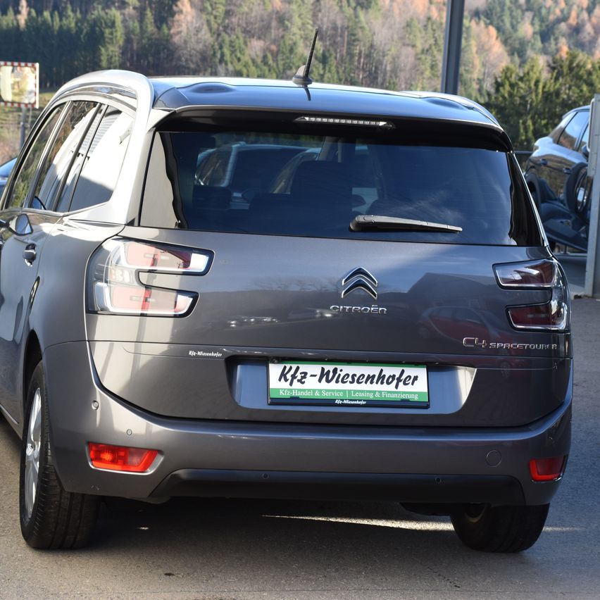 Die Rückseite eines grauen Citroen C4 Spacetourer SUV steht auf einem Parkplatz mit einem Nummernschild, das 'Kfz-Wiesenhofer' liest. Bäume sind im Hintergrund.