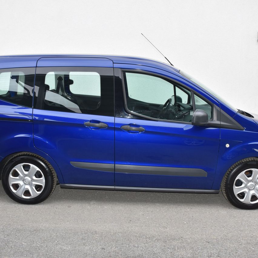 Ein blauer Van ist vor einer weißen Wand geparkt und zeigt sein schlankes Design, Silberfelgen und aerodynamische Merkmale.