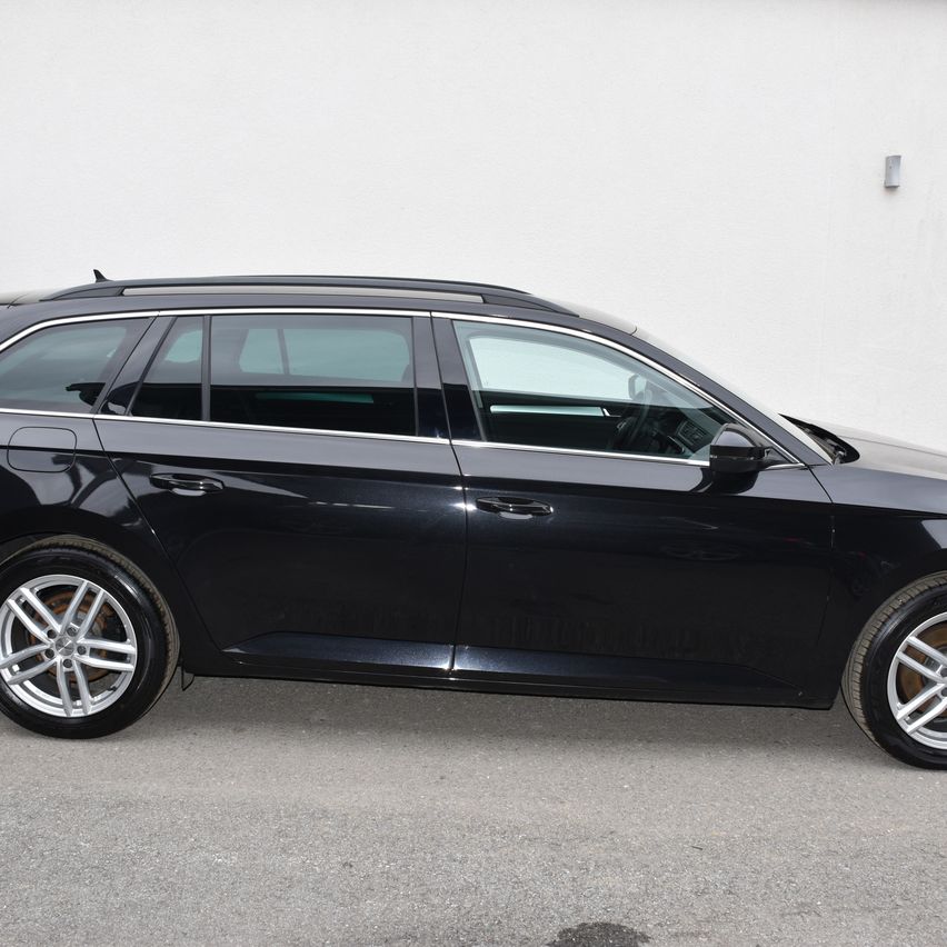 Ein schwarzer Kombi mit Leichtmetallrädern steht vor einer weißen Wand. Das Auto hat auf beiden Seiten Silberfelgen.