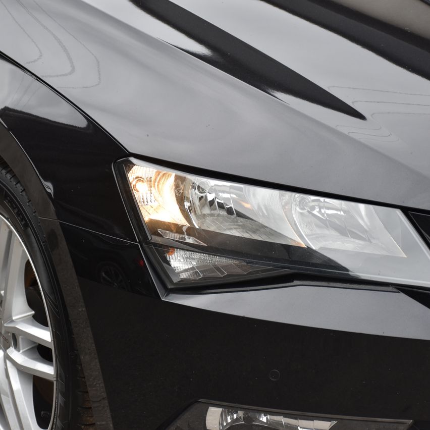 Nahaufnahme eines schwarzen Autos mit eingeschaltetem Scheinwerfer, Rad und Stoßfänger.