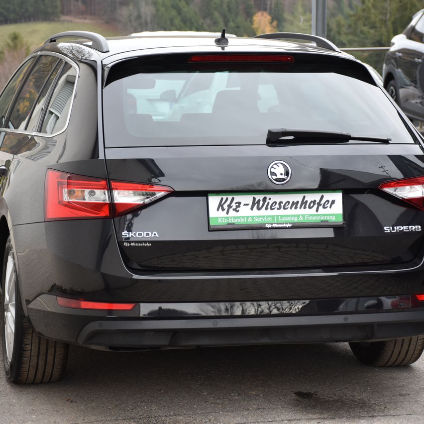 Ein schwarzer Skoda Superb ist auf einer Straße geparkt und zeigt von hinten ein grünes Nummernschild mit 'Kfz-Wiesenhofer' und 'Kfz-Handel & Service | Leasing & Finanzierung'.