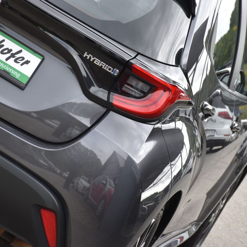 Nahaufnahme der Heckansicht eines schwarzen Autos mit einem Nummernschild, einem roten Rücklicht und dem Wort 'Hybrid' auf dem Kofferraum.