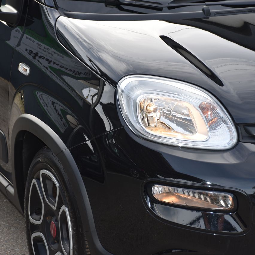 Eine Nahaufnahme eines schwarzen Autos mit eingeschalteten Scheinwerfern, die einen schlanken und polierten vorderen Stoßfänger zeigt.
