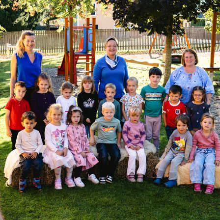 Eine Gruppe von Kindern und drei Lehrern posiert in einem Park mit einem Spielplatz im Hintergrund.