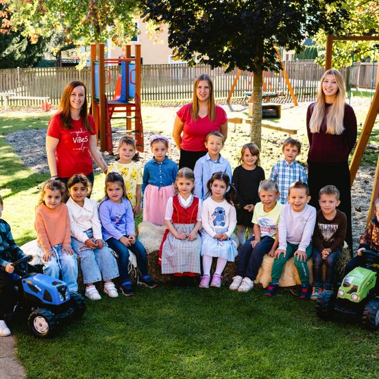 Eine Gruppe junger Schüler und drei Lehrerinnen posiert für ein Foto im Freien in der Nähe einer Spielanlage.