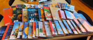 Ein langer Tisch in einem Raum mit Büchern in einer Pyramidenform angeordnet, dekoriert mit Tannenzapfen und Grün. Neben dem Tisch stehen Stühle und ein Monitor. Draußen am Fenster ist ein Auto zu sehen.