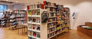 Eine Bibliothek mit mehreren Regalen voller Bücher und Zeitschriften. Ein Tisch hält Bücher. Ein anderes Regal hält Brettspiele.