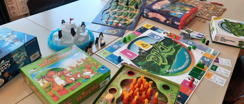 Ein Tisch mit verschiedenen Brettspielen, darunter 'Häschen', 'Zwergenwerk' und 'DRU', mit Spielfiguren und Karten aufgebaut.