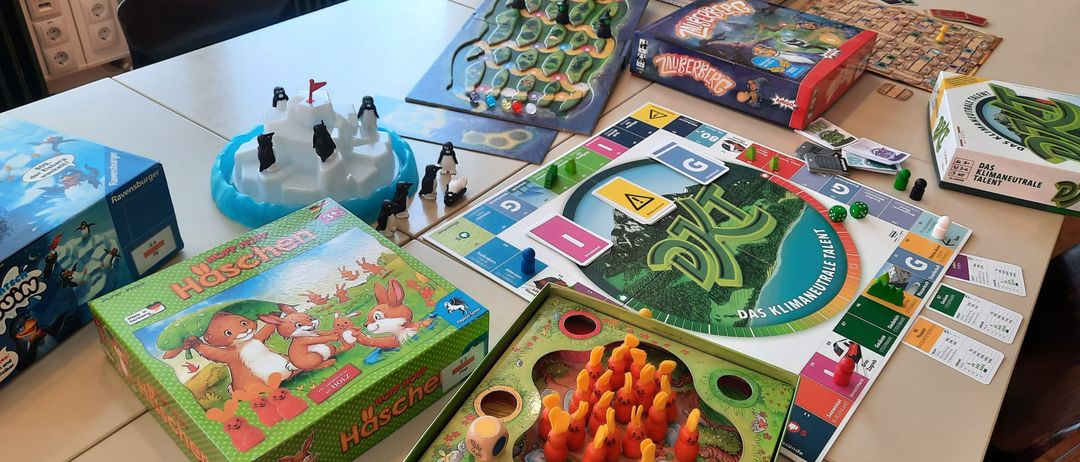 Ein Tisch mit verschiedenen Brettspielen, darunter 'Häschen', 'Zwergenwerk' und 'DRU', mit Spielfiguren und Karten aufgebaut.