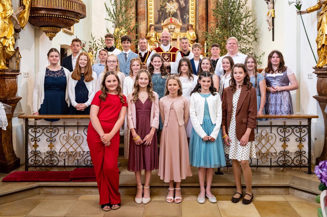 Eine Gruppe von Menschen, darunter Kinder und Erwachsene, posiert für ein Foto vor einem Kirchenaltar mit einer goldenen Statue.