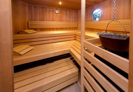 Eine hölzerne Sauna mit Bänken, einem runden Fenster, einer Uhr und einem hängenden Topf.