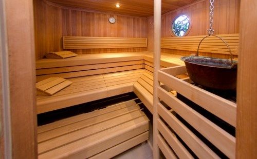 Eine hölzerne Sauna mit Bänken, einem runden Fenster, einer Uhr und einem hängenden Topf.