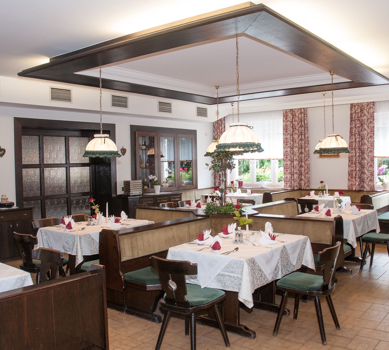 Ein Innenraum eines traditionellen deutschen Restaurants. Es verfügt über Holzbänke, weiße Tischdecken und Blumendekorationen. Die Einrichtung ist elegant und gemütlich.