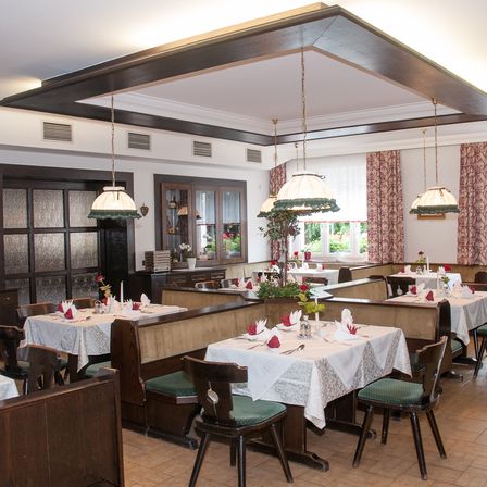 Ein Innenraum eines traditionellen deutschen Restaurants. Es verfügt über Holzbänke, weiße Tischdecken und Blumendekorationen. Die Einrichtung ist elegant und gemütlich.