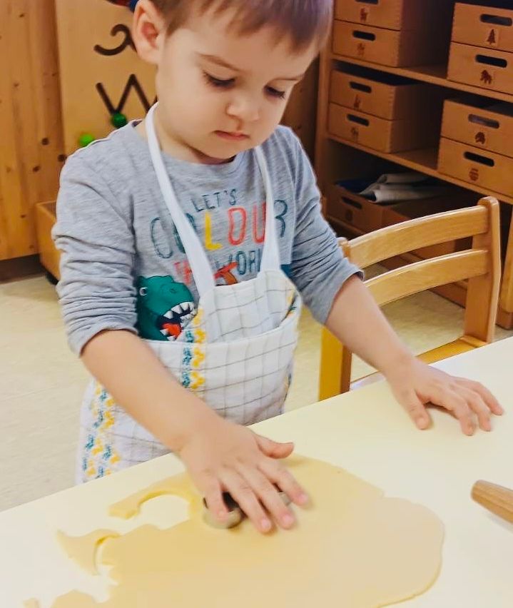 Ein junger Junge in einer Schürze konzentriert sich darauf, Teig mit einem Nudelholz auf einem Tisch auszurollen.
