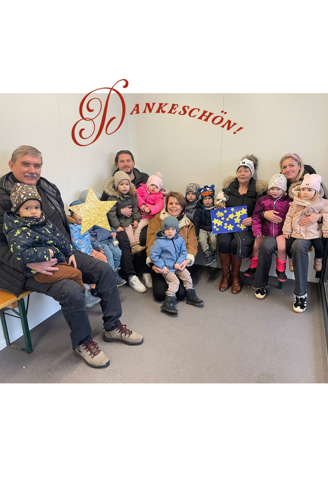 Eine Gruppe von Erwachsenen und Kindern posiert für ein Foto in einem Raum, dessen Wand Dankeschön trägt. Einige halten Schilder mit gelben Sternen.
