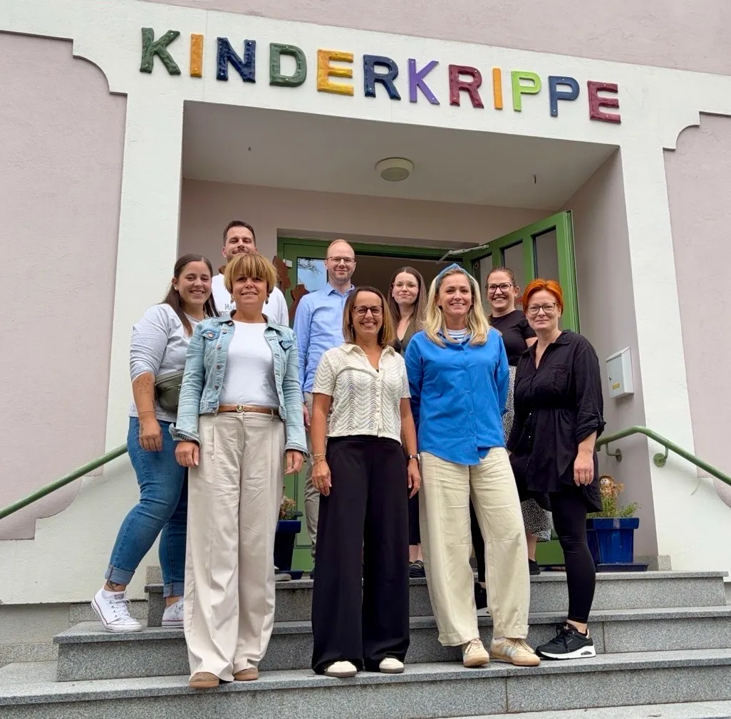 Eine Gruppe von Menschen steht auf den Stufen vor einem Gebäude mit dem Schild Kinderkrippe.