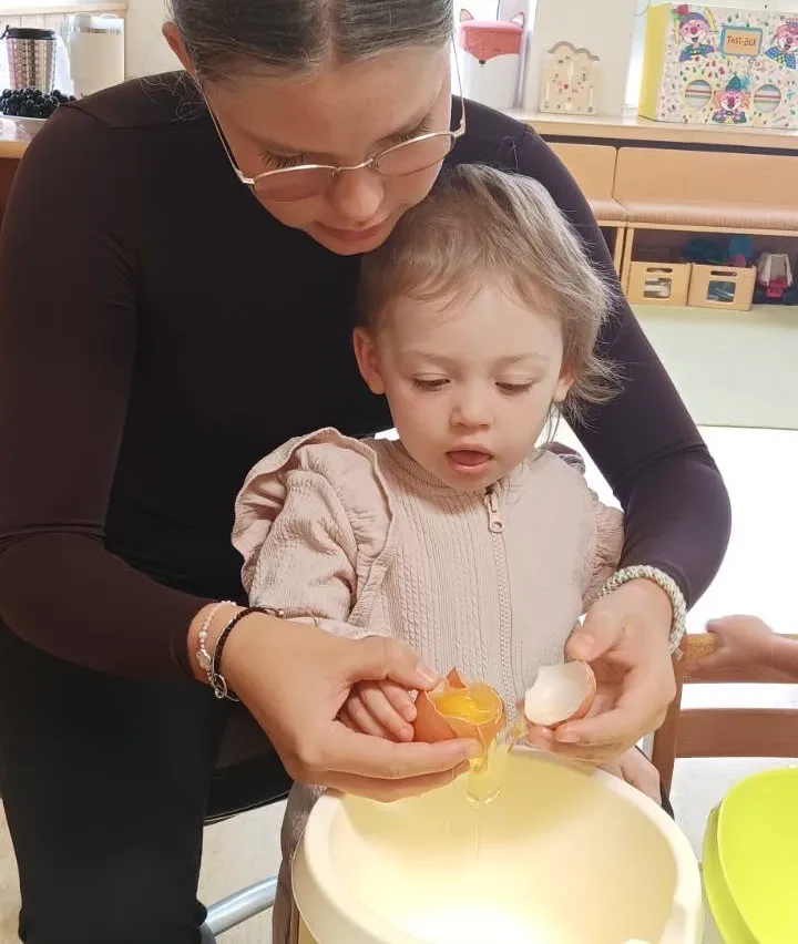 Eine Frau mit Brille hilft einem kleinen Mädchen, Eigelb vom Eiweiß in einer Schüssel zu trennen.