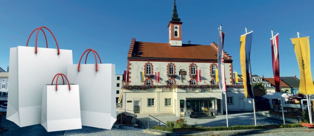 Ein Gebäude mit einem braunen Dach und Turm, geschmückt mit Flaggen, hat eine Ladenfront mit einem Schild, und zwei Einkaufstüten sind davor platziert.