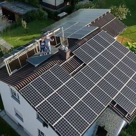 Eine Luftaufnahme eines Hauses mit Solarpanelen auf dem Dach. Zwei Personen stehen auf dem Dach.