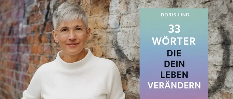 Eine Frau mit kurzem weissem Haar und Brille trägt ein weisses Rollkragenshirt und steht neben einem Buch mit dem Titel '33 Worte, die dein Leben verändern können'.
