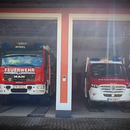 Zwei Feuerwehrfahrzeuge sind in einer Feuerwache geparkt. Der MAN-Lkw hat das Kennzeichen FW 254 SL und der Mercedes-Benz-Lkw hat das Kennzeichen FW 326 SL.