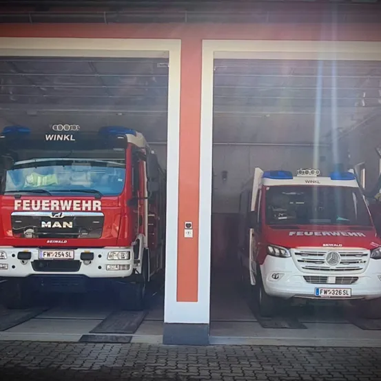 Zwei Feuerwehrfahrzeuge sind in einer Feuerwache geparkt. Der MAN-Lkw hat das Kennzeichen FW 254 SL und der Mercedes-Benz-Lkw hat das Kennzeichen FW 326 SL.