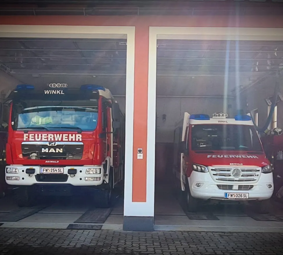 Zwei Feuerwehrfahrzeuge sind in einer Feuerwache geparkt. Der MAN-Lkw hat das Kennzeichen FW 254 SL und der Mercedes-Benz-Lkw hat das Kennzeichen FW 326 SL.