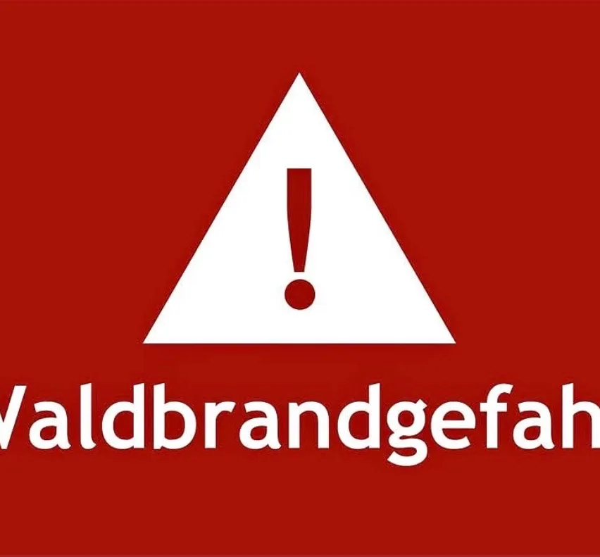Ein roter Hintergrund mit einem weißen Dreieck, das einen Ausrufepunkt enthält, und dem Wort 'Waldbrandgefahr' darunter.