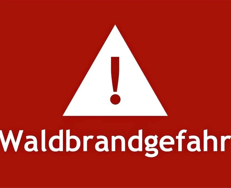 Ein roter Hintergrund mit einem weißen Dreieck, das einen Ausrufepunkt enthält, und dem Wort 'Waldbrandgefahr' darunter.