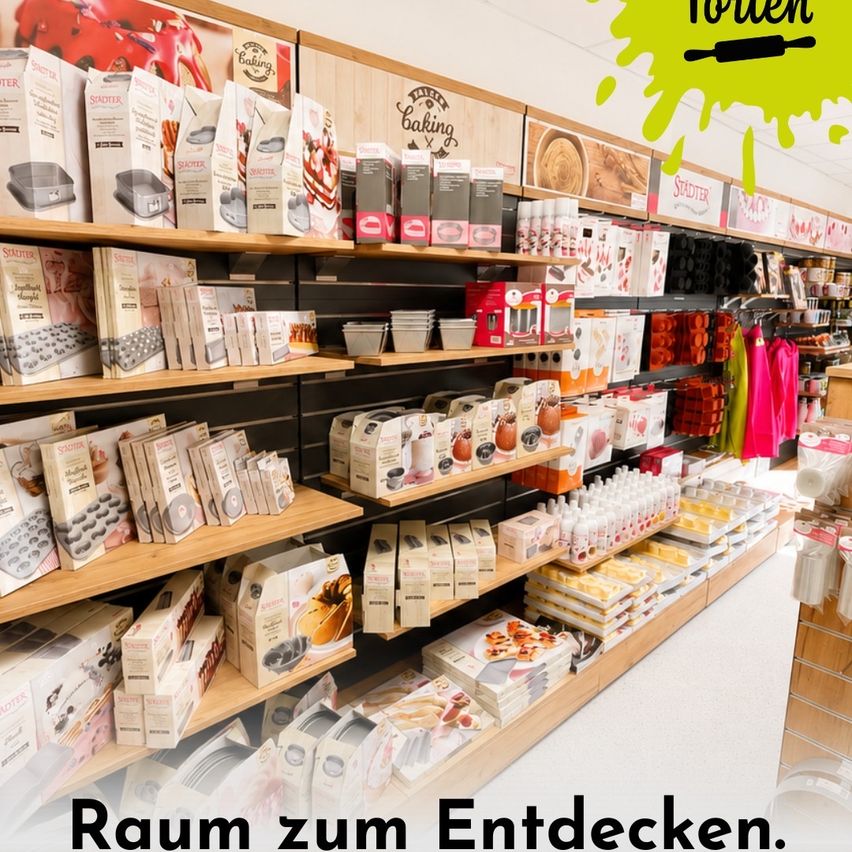 Ein Bäckereibedarfsladen mit verschiedenen Backwerkzeugen und Zutaten, die ordentlich auf Regalen angeordnet sind. Der Laden hat ein helles und sauberes Erscheinungsbild mit dem Slogan 'Raum zum Entdecken' unten.