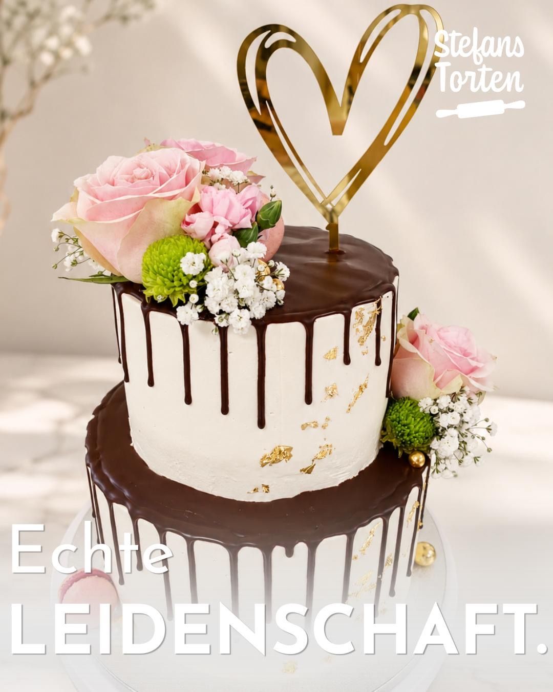 A two-tiered chocolate cake with white frosting, chocolate drips, and gold accents, topped with pink roses and other flowers, and a heart-shaped gold topper. The cake is placed on a white surface with the text 'Echte Leidenschaf'.