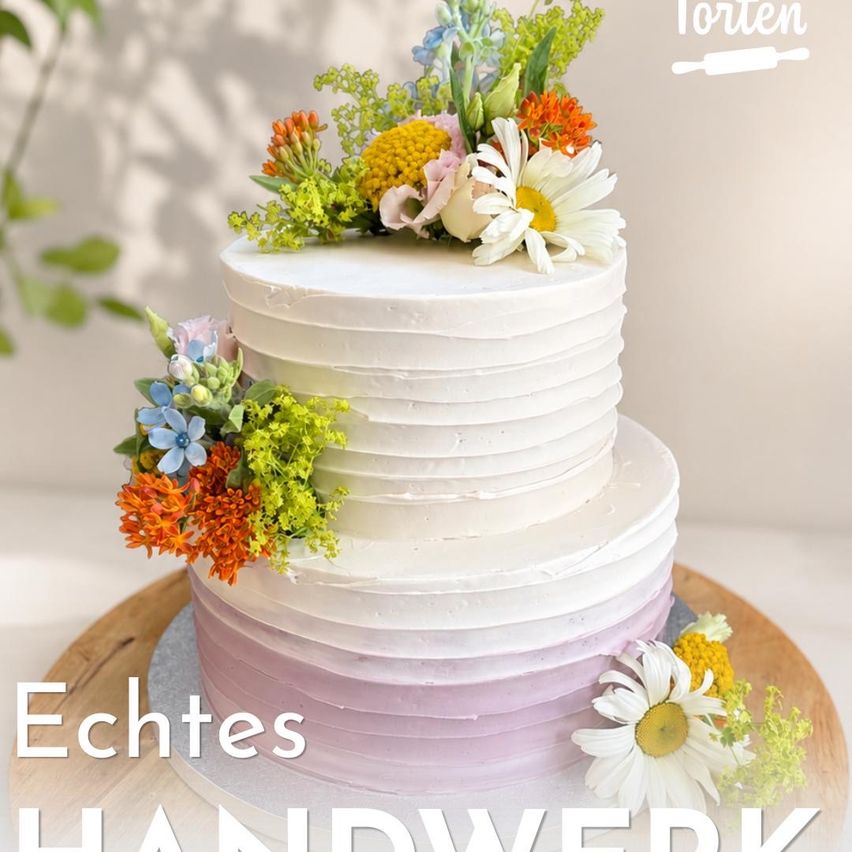 A three-tiered cake with white frosting and colorful flowers on top, displayed on a wooden board with the words 'Echtes Handwerk'.
