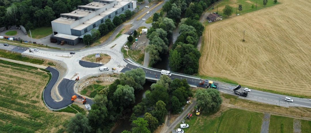 Ein Luftbild einer Stadt mit vielen Gebäuden, einer großen Fabrik, einer Straße mit Fahrzeugen, einer Brücke und einem großen Feld.